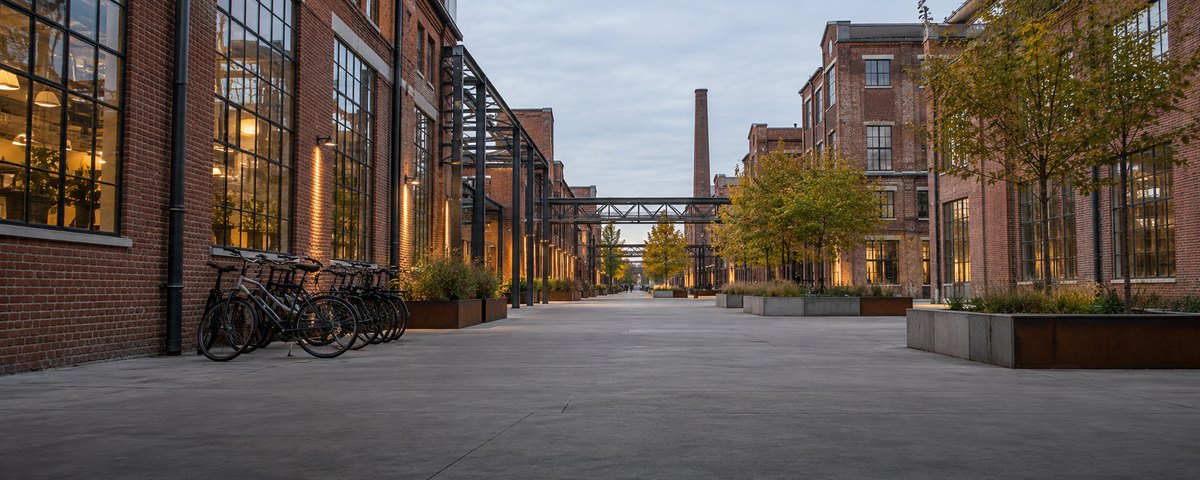Converted red-brick former electronics factory buildings with tall steel-framed windows along a wide pedestrian strip in Eindhoven, the Netherlands